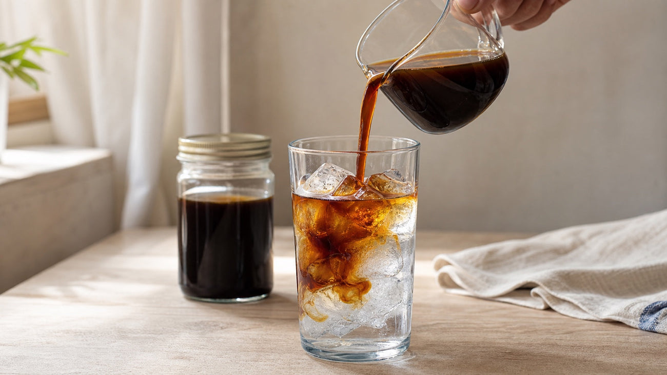 Cold brew concentrate is poured into a glass of water and ice, creating dark coffee layers.