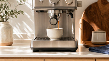 A compact home espresso machine pulls a double shot with rich crema into a small ceramic cup.