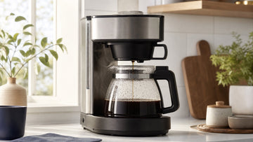 A home drip coffee maker brews fresh coffee into a glass carafe on a sunlit kitchen counter.