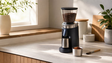 A home burr grinder sits beside a dosing cup filled with evenly ground fresh coffee.
