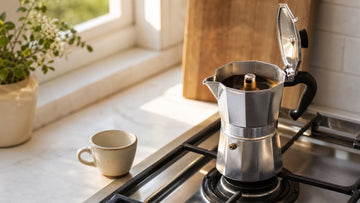 Fresh coffee rises into the upper chamber of a stainless moka pot on a stovetop.