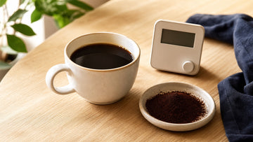 Black coffee sits beside a timer and a dish of finely ground coffee used to illustrate over-extraction.
